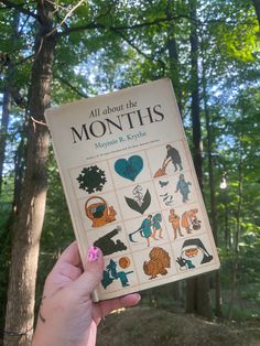 someone holding up a book in front of some trees and bushes with the title all about the months