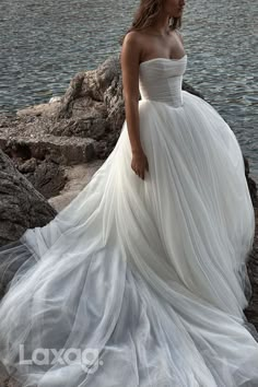 a woman in a white dress standing on rocks by the water with her hands behind her back