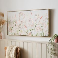 a painting hanging on the wall next to a chair with a blanket and potted plant