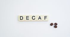 the word decaf spelled with scrabble letters next to coffee beans on a white surface