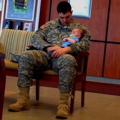 a soldier holding a baby in his lap while sitting on a chair next to a couch