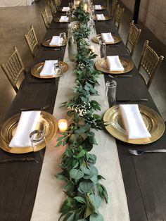 a long table set with place settings and greenery on the runner, along with candles