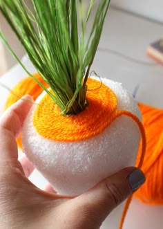 a hand holding a ball of yarn with grass growing out of it, on top of a table