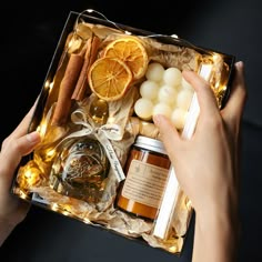 a person holding a box filled with oranges, candles and other items in it