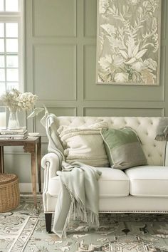 a white couch sitting in front of a window next to a table with flowers on it