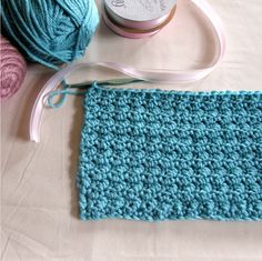 a crocheted blue blanket next to a ball of yarn and a spool of thread