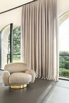 a living room with a large window and a chair in front of the curtained windows