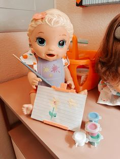 a baby doll sitting on top of a desk next to a notepad and brush