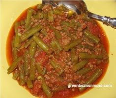 a yellow plate topped with green beans covered in chili and meat next to a spoon