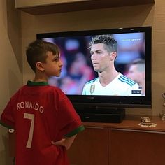 a young boy standing in front of a tv watching soccer on it's screen