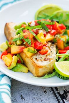 a white plate topped with fish and veggies next to a slice of lime