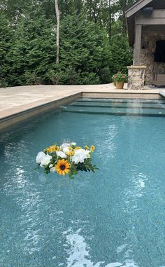 flowers are placed on the edge of a pool in front of an outdoor fireplace and grill