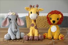 three crocheted stuffed animals sitting next to each other on a wooden table in front of a wall