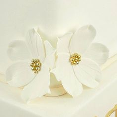 two white flowers sitting on top of a cake covered in frosting and gold decorations