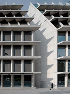 a person walking on the sidewalk in front of two buildings that are made of concrete