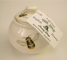 a white jar with a yellow and black bee painted on it's lid is next to a tag that says, the hive