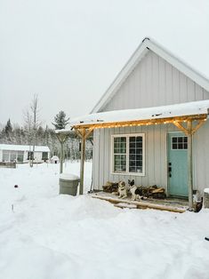 two dogs sitting on the porch of a small white house in the snow with christmas lights