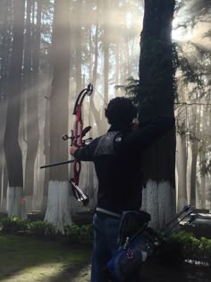 a man holding a bow and arrow in the woods on a foggy day with sun shining through the trees