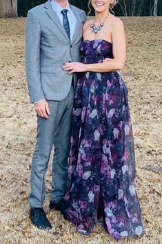 a man and woman standing next to each other in front of some trees with leaves on the ground