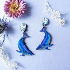 These humpback whale and shell earrings are detailed works of art for whale watchers, nature lovers, and dreamers! These original earrings are digitally illustrated and laser-etched on cherry wood featuring seashells with a playful hanging whale. The whale is meticulously hand-painted in a deep sea color palette of blues with blushes of purple and grey. The whale hangs from a swirling white and blue sea shell, completing this ocean-themed look! Super lightweight and one-of-a-kind, these whales a Sea Color Palette, Whale Earrings, Wood Earrings Stud, Sea Colour, Wood Studs, The Whale, Kraft Gift Boxes, Humpback Whale, Hand Painted Wood