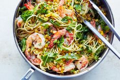 a pan filled with pasta and shrimp on top of a white table next to a fork