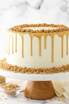 a white cake with caramel drizzle on top sitting on a wooden stand