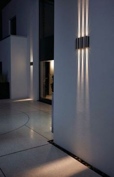 a white wall with three lights on it and a black door in the background at night