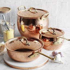 three copper pots and pans on a marble table