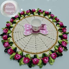 a crocheted doily with a coffee cup on it and pink flowers around the edge