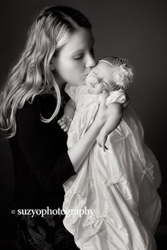 a woman holding a baby in her arms and kissing it's face with the other hand