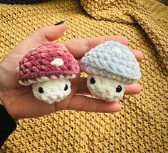 two small crocheted mushrooms are held in someone's hand, one is wearing a knitted hat