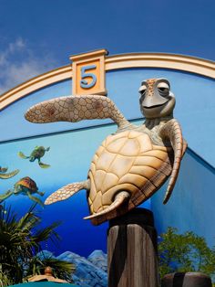 a statue of a turtle on top of a wooden post in front of a mural