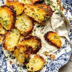 a blue and white plate topped with potatoes covered in ranch dressing next to a spoon