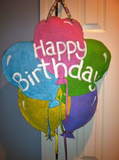 three balloons with happy birthday written on them hanging from a door hanger in front of a white door