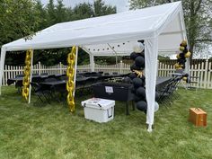 a white tent with black and gold balloons on the grass next to some picnic tables