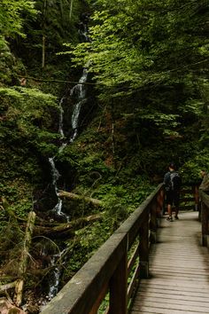 two people walking across a wooden bridge near a waterfall