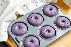 a muffin pan filled with purple donuts on top of a wooden table