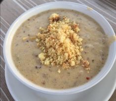 a white bowl filled with soup and crumbs on top of a wooden table