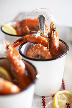 two cups filled with shrimp on top of a table next to lemon wedges and a knife