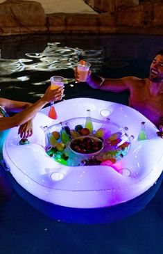 two people are sitting in the pool with drinks and snacks on an inflatable float