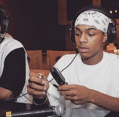 two young men sitting at a table with headphones on and looking at their cell phones