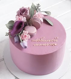 a pink cake with flowers and writing on it sitting on a white table next to a cupcake