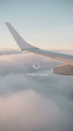 an airplane flying above the clouds with a holiday is coming message on it's side