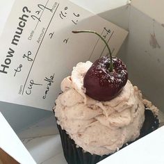 a cupcake with cream frosting and a cherry on top in a white box