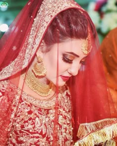 a woman in a red and gold wedding outfit is looking down at her hands while she wears