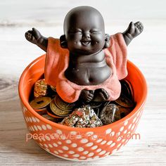 a small buddha statue sitting in a bowl filled with coins