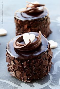 two cakes with chocolate frosting and white hearts on top are sitting on a table