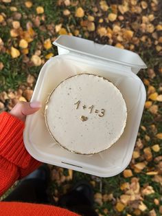 a person holding up a white cake in a plastic container with the number thirteen on it