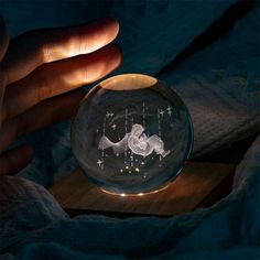 a hand holding a glass ball with stars in the sky on it and a light inside