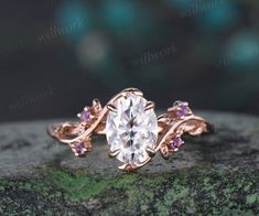 a ring with an oval cut diamond surrounded by pink sapphires on top of a rock